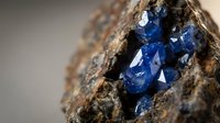 Raw blue sapphire crystals embedded in natural rock matrix showing brilliant faceted gemstone formation in earth mineral specimen for geology study.