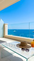 Luxury hotel balcony with sea view, summer hat, sunglasses and cocktail on glass table, yachts on blue ocean horizon on sunny day.