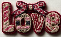 Handmade embroidered love text with decorative bow in pink and burgundy threads on fabric background for romantic crafts and Valentine projects.