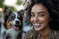 Happy young African American woman with curly hair smiling with her Australian Shepherd dog outdoors in natural sunlight creating joyful pet owner moment.