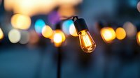 Glowing vintage Edison bulb with warm light against blurred bokeh background creates atmospheric mood lighting for outdoor evening events and celebrations.