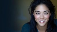 Young Asian woman with bright genuine smile and natural makeup wearing dark blue top against blurred background, looking directly at camera with confident expression.