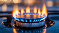 Blue gas flame burning on modern kitchen stove burner with bokeh lights in background, close up view showing energy consumption and cooking concept.