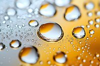 Clear water drops on metallic gold and silver surface create abstract macro photography pattern with reflective spherical shapes and natural light effects.