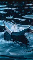 White paper boat floating on dark blue water surface with ripples and water drops, creating atmospheric mood in macro photography. Symbolic journey concept.