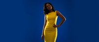 Young African American woman in bright yellow dress posing confidently against clear blue sky background for fashion and lifestyle photography.