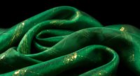 Luxurious emerald green silk fabric with golden glitter accents flowing in elegant curves against black background for premium textile design projects.