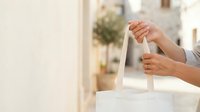 Woman holding white fabric tote bag with handles, outdoor urban setting with blurred buildings background, suitable for retail, shopping, eco-friendly products, branding mockups.