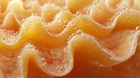 Golden wavy pasta with textured surface and flowing curves creates abstract food pattern for culinary designs and cooking backgrounds.