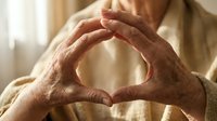 Elderly hands forming heart shape gesture expressing love and care in warm indoor setting with soft natural lighting.