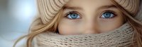 Young blonde woman with striking blue eyes wearing beige knit winter hat and scarf covering lower face. Cold weather fashion portrait with soft lighting.