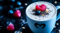 Creamy latte topped with fresh raspberries, blueberries and chia seeds in blue ceramic cup with heart design against dark background, romantic mood.