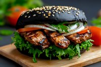 Grilled chicken burger with black charcoal bun, fresh vegetables, lettuce, tomatoes and onions on wooden board. Close up view of gourmet sandwich for menu design.