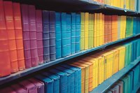 Colorful rainbow arrangement of books on library shelves, organized by spectrum from red to yellow to blue and green, creating vibrant rows of knowledge.