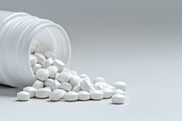 White round pills spilling from plastic prescription bottle on light gray background, pharmaceutical concept for medical and healthcare industry.