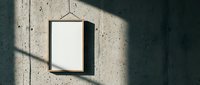 Empty wooden frame hanging on concrete wall with dramatic shadow patterns from window light creating minimalist interior design mockup space.
