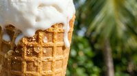 Soft serve vanilla ice cream melting on crispy waffle cone with blurred green foliage background, perfect for summer food and dessert marketing materials.