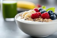 Healthy breakfast bowl with yogurt, granola, fresh berries, banana slices and mint leaf, served with green smoothie and fruit for balanced nutrition.