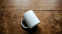 White ceramic coffee mug on rustic wooden table surface for mockup design and branding projects.