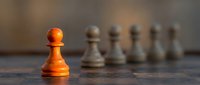 Orange pawn standing out from gray pawns on chessboard, symbolizing leadership, uniqueness, and strategic business success.