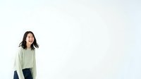 Young East Asian woman with shoulder-length dark hair wearing a light sage green cardigan over a dark top, standing against a neutral white background with copy space.