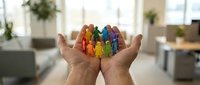 Hands holding colorful wooden figures representing diversity, inclusion and teamwork in modern office environment for business concepts.
