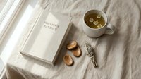 Mindfulness meditation setup with herbal tea, wooden stones, sage bundle and inspirational book on linen fabric for wellness and self-care practices.