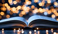 Open book with blurred warm bokeh lights creating magical atmosphere. Pages spread against dark background with glowing string lights creating dreamy reading ambiance.