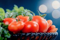 Fresh red tomatoes with green stems in wicker basket on blue background with bokeh lights. Organic vegetables for healthy cooking and nutrition concepts.