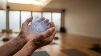 Elderly hands cupped holding clear water in modern kitchen interior with natural lighting and wooden surfaces for health and wellness concepts.