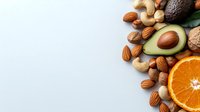 Fresh organic avocado, orange slice, and assorted nuts including almonds, cashews, and walnuts arranged on white background, healthy fats and protein sources.
