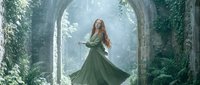 Young woman with long red hair in flowing green dress dancing in mystical stone archway covered with ivy and moss in enchanted forest setting.