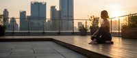 Young woman practicing meditation on urban rooftop terrace at golden hour sunset with city skyline background for wellness and mindfulness lifestyle.