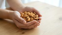 Hands holding handful of roasted almonds on wooden table surface. Healthy snack and nutrition concept for food, wellness, and dietary content.