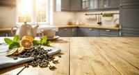 Modern kitchen counter with green tea leaves, dried orange slices and fresh mint herbs on wooden cutting board. Cozy cooking space background for healthy lifestyle.