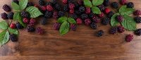 Fresh blackberries and raspberries scattered on rustic wooden surface with green leaves, ideal for food styling, recipe blogs, and culinary design projects.