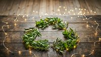 Fresh herb wreath with rosemary and greenery on rustic wooden background with warm fairy lights creating cozy kitchen decor for cooking and culinary arts.