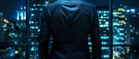 Businessman in dark suit standing against illuminated night city skyline with glowing blue windows, rear view. Modern urban corporate concept.