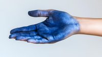 Hand covered in blue pigment or dye against white background, showing palm up gesture for creative arts, painting, or dyeing process.