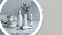 Minimalist white cosmetic bottles and jars arranged on marble surface with eucalyptus branch in modern circular mirror frame for skincare branding.