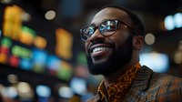 Young African American businessman with beard and glasses smiling confidently against blurred city lights background, wearing stylish plaid blazer and patterned shirt.