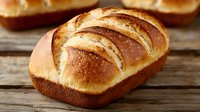 Freshly baked artisan bread loaf with golden crust and distinctive scoring pattern on rustic wooden surface, showcasing traditional baking craftsmanship.
