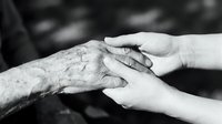 Compassionate caregiver hands gently holding elderly person's wrinkled hand in black and white, showing intergenerational care and support.