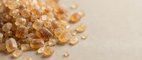 Brown sugar crystals scattered on neutral surface, suitable for food photography, baking content, sweetener concepts, and culinary backgrounds.
