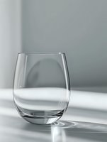 Empty stemless wine glass on light gray background with dramatic shadow and sunlight creating minimalist composition. Clean glassware for beverage photography.
