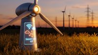 Smart wind turbine with IoT connectivity display at sunset in renewable energy farm with power lines and golden wheat field for sustainable technology concepts.