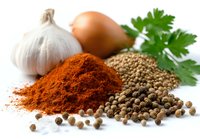 Fresh cooking ingredients with vibrant red paprika powder, coriander seeds, allspice, garlic bulb, onion and parsley on white background for culinary use.