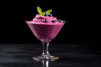 Purple berry smoothie bowl in elegant glass garnished with fresh mint and blueberries on dark background for healthy breakfast dessert presentation.