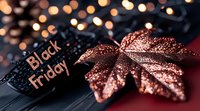Glittering rose gold maple leaf decoration with Black Friday text against dark background with bokeh lights, creating festive holiday shopping atmosphere.