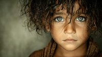 Young child with curly hair and striking blue eyes looking directly at camera with serious expression in natural lighting for emotional storytelling content.